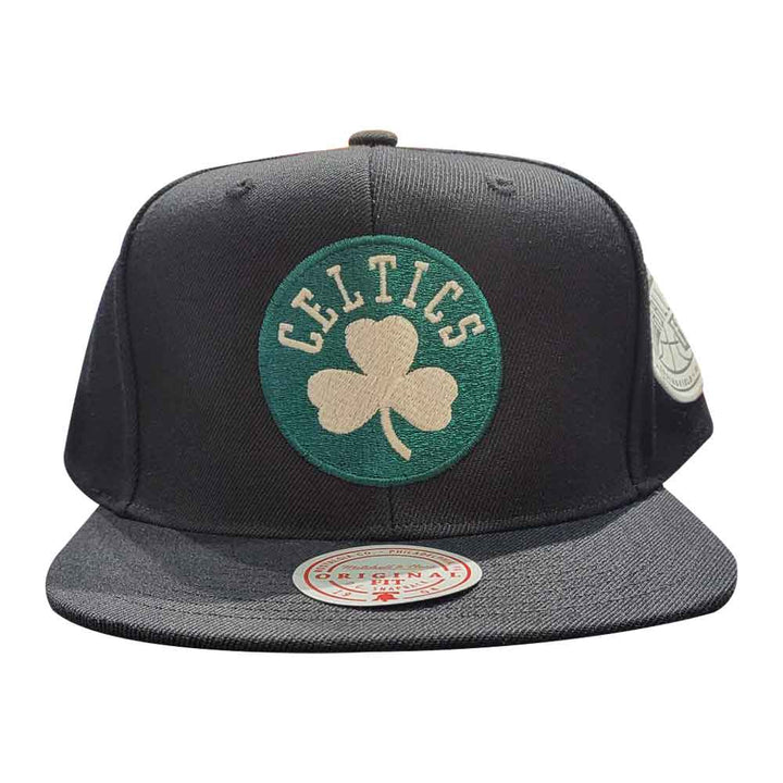 The Basketball Hall of Fame Celtics Mitchell & Ness Cap is black with a green circular “Celtics” patch and a cream shamrock on the front. It features a Hall of Fame round sticker on the brim.