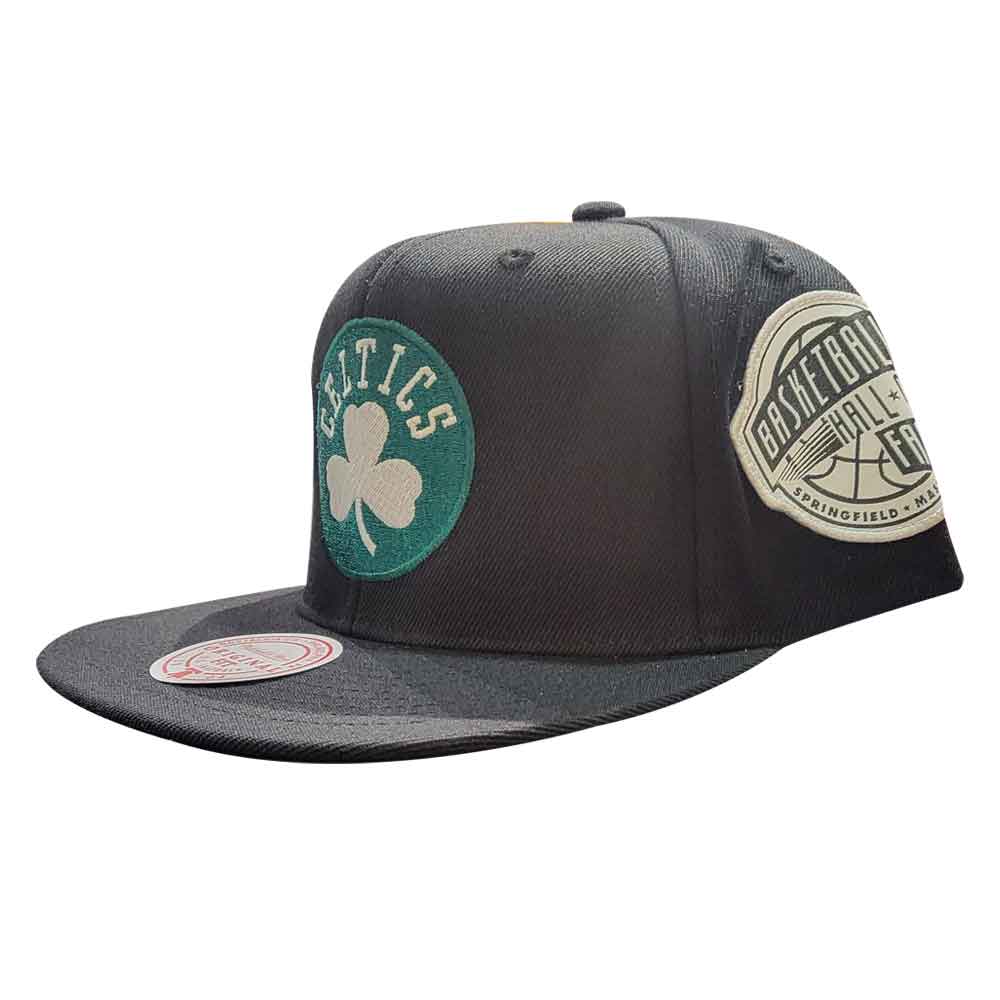 The Basketball Hall of Fame Celtics Mitchell & Ness Cap is a black, flat-brimmed hat with a green and white shamrock logo on the front and a side “Basketball Hall of Fame” patch.