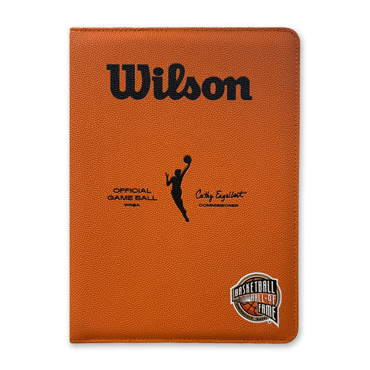 The Basketball Hall of Fame x Wilson WNBA Padfolio is a brown portfolio styled like a basketball, with the Wilson logo, a player silhouette, signature, and Basketball Hall of Fame logo on the bottom right corner.