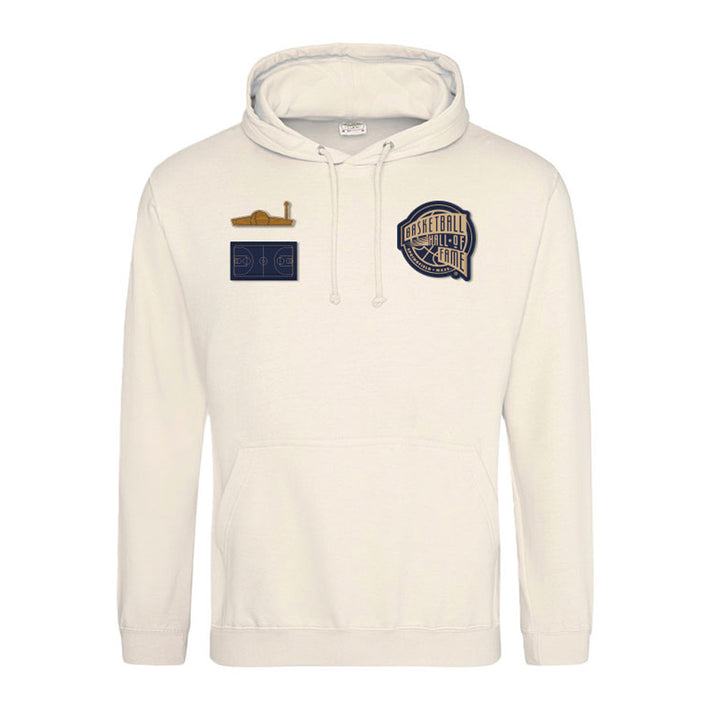 The Basketball Hall of Fame® 2026 Enshrinement Hooded Sweatshirt in cream features three chest patches: a basketball court diagram, a golden brown whistle, and a large "Basketball Hall of Fame Champions Club" patch.