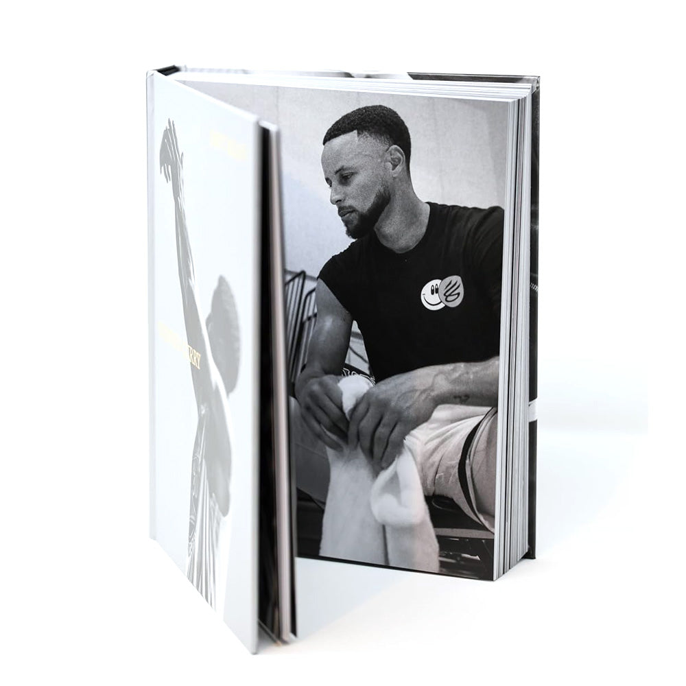 An open hardcover "Shot Ready" book reveals a black-and-white photo of a bearded man sitting with a towel. The cover features a silhouette with one arm raised, capturing the Shot Ready philosophy of success.