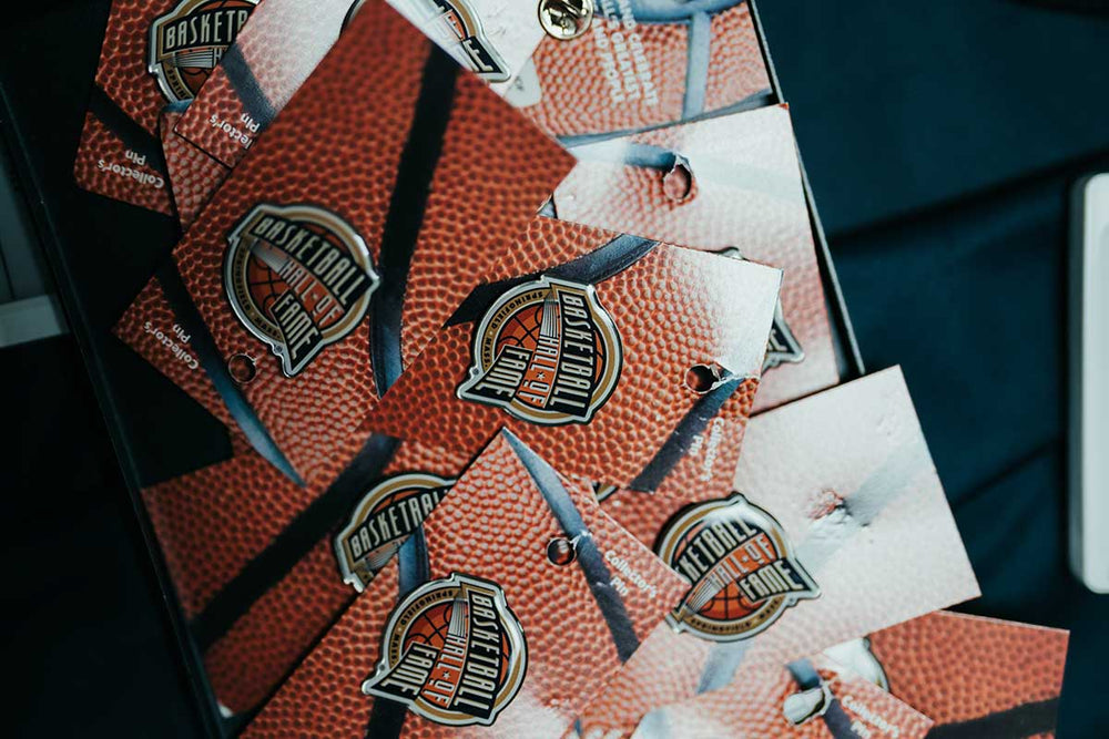 A stack of Basketball Hall of Fame Pin and Card sets featuring a basketball texture and the official Hall of Fame logo, closely arranged on a dark surface—an ideal unique basketball gift or collectible souvenir enamel pin for fans and enthusiasts alike.