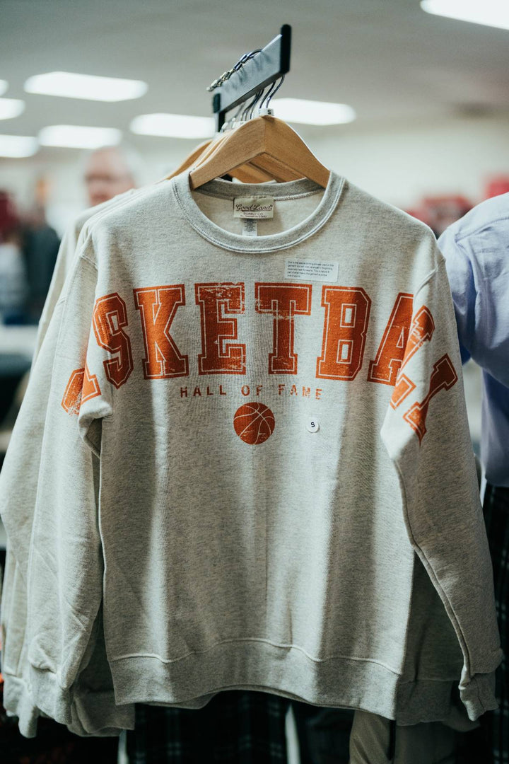 The Basketball Hall of Fame® Spread Arms Fleece Sweatshirt is a gray sweatshirt displayed on a hanger, featuring "BASKETBALL HALL OF FAME" and a basketball graphic printed in bold orange and white letters—perfect for fans who appreciate basketball history.