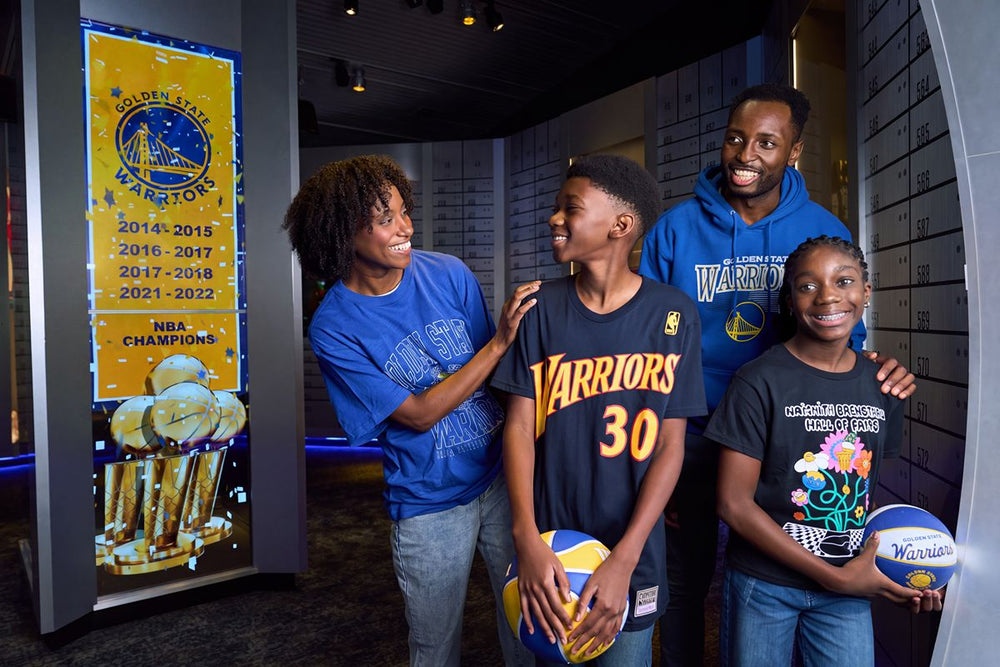 A family wearing NBA Golden State Warriors Steph Curry Jersey T-Shirts stands in front of a display case showing the team’s championship years and trophies.
